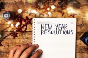 person-writing-new-years-resolutions-on-wood-desk-red-star-ornaments