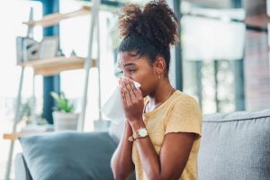 woman-sits-on-couch-sneezes-into-kleenex