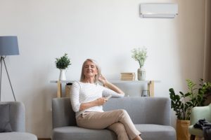 middle-aged-woman-sits-on-sofa-with-mini-split-behind-her