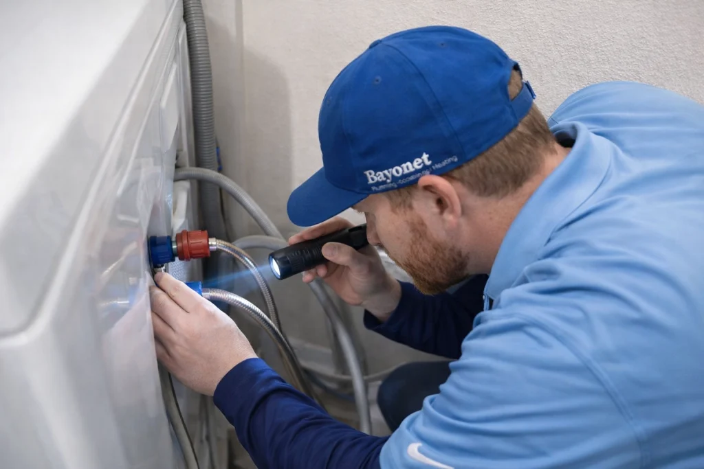 A Bayonet plumber inspecting hoses of a washing machine.